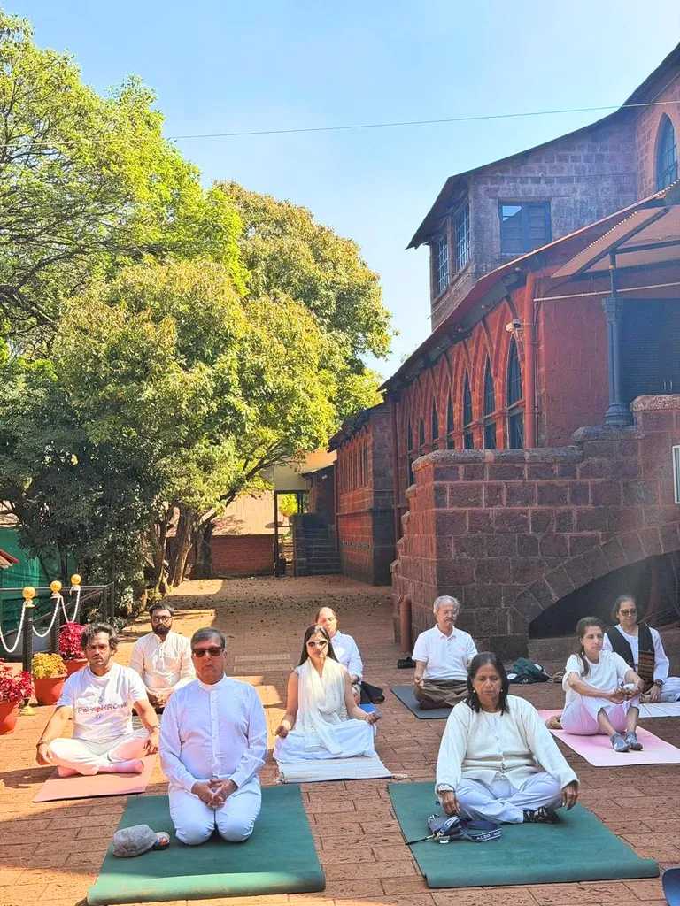 Participants in white sitting in meditation on mats in the sunlit club courtyard