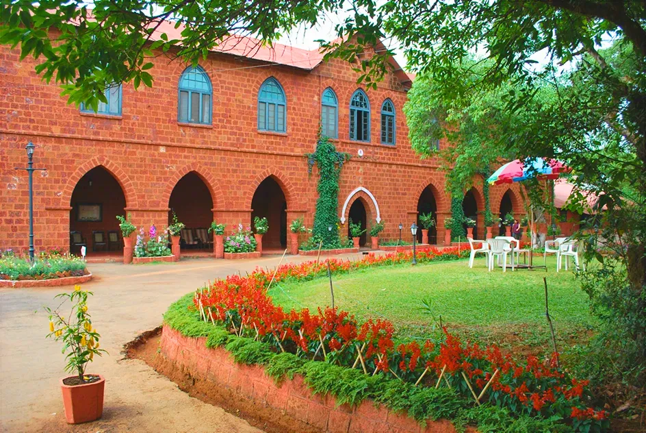 The arched red-stone façade of The Mahabaleshwar Club behind a bed of red flowers